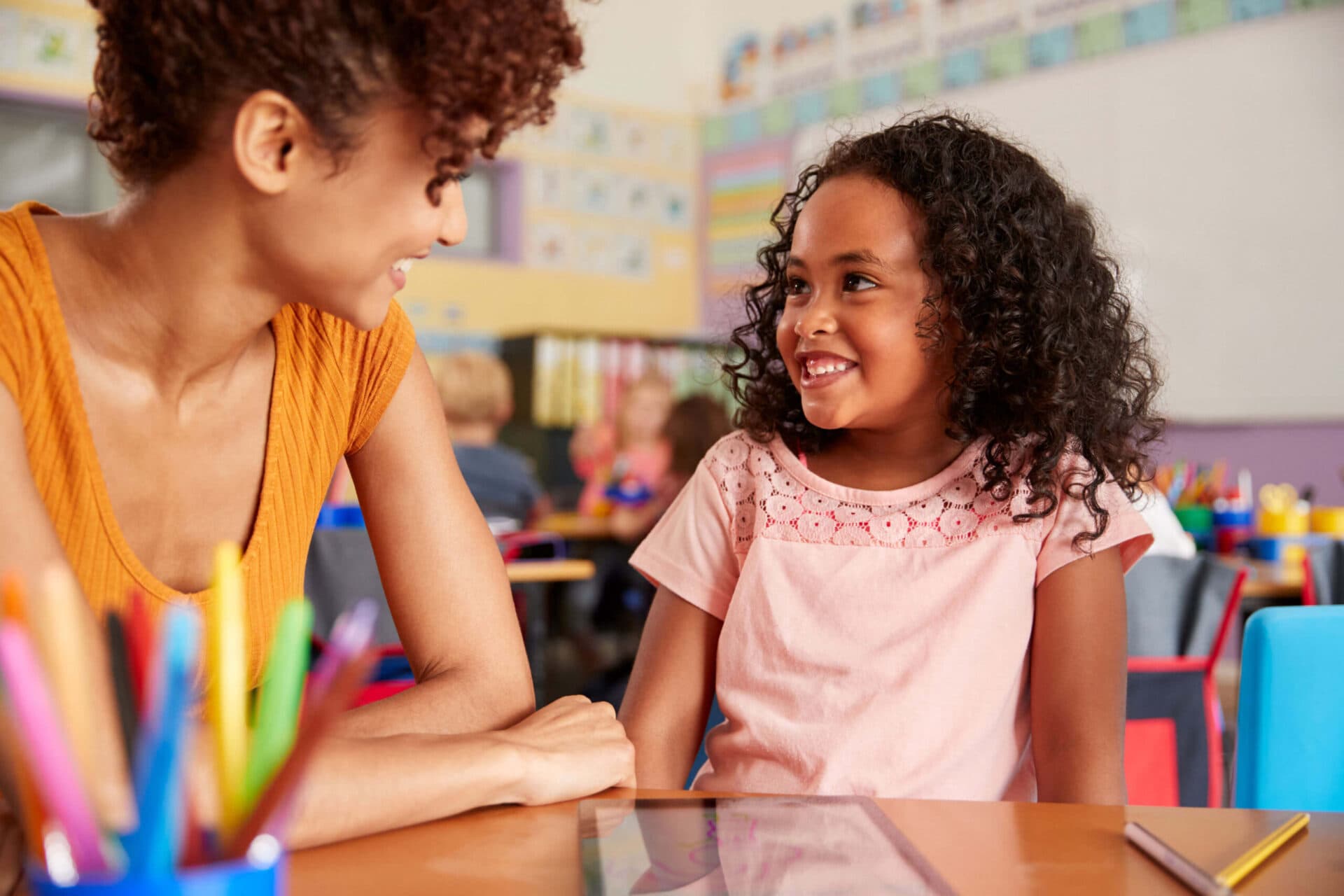A teacher and a child smiling at each other in a Little People’s Landing classroom